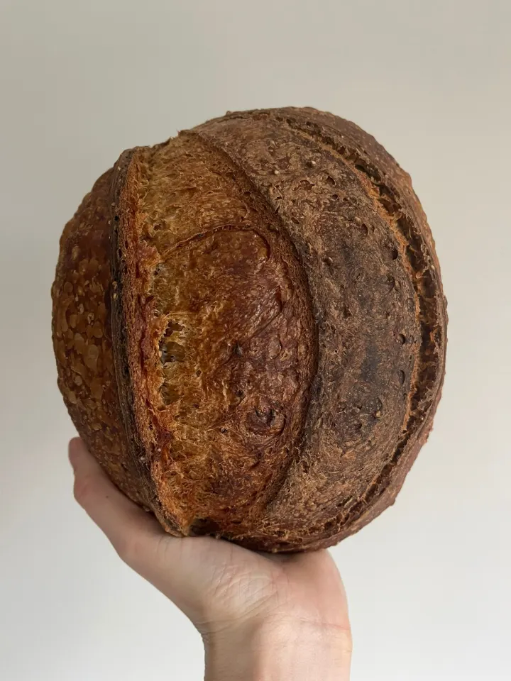 A round granary crunch sourdough loaf held up in one hand
