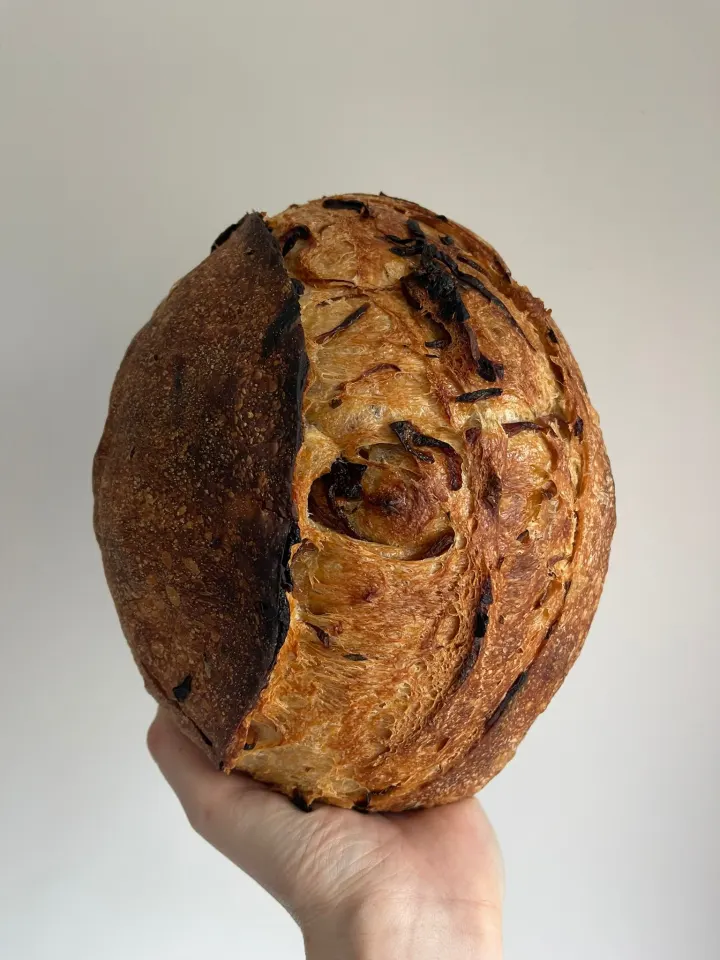 A round rosemary and caramelised red onion sourdough loaf held up in one hand