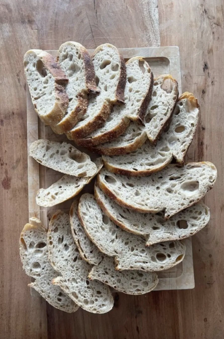 Slices of open-crumb white sourdough fanned out on a wooden board